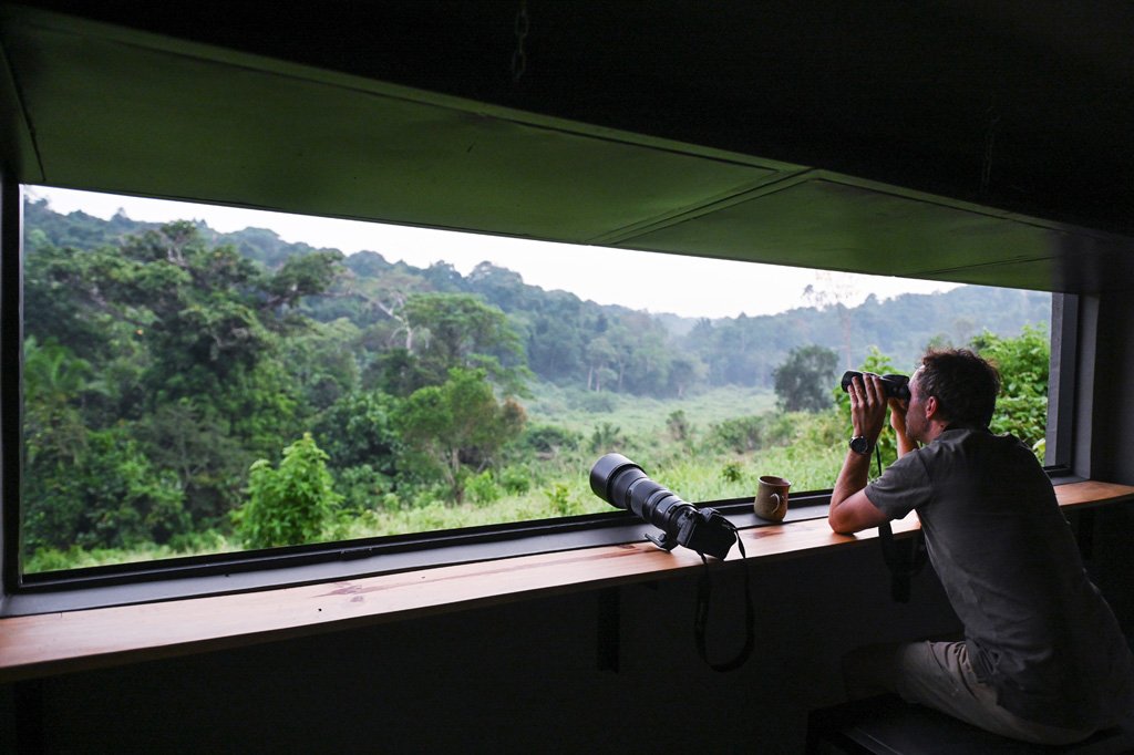 What to Pack for Kibale National Park 21 Visitor using binoculars beside a telephoto camera lens overlooking the forest near Kibale National Park Uganda