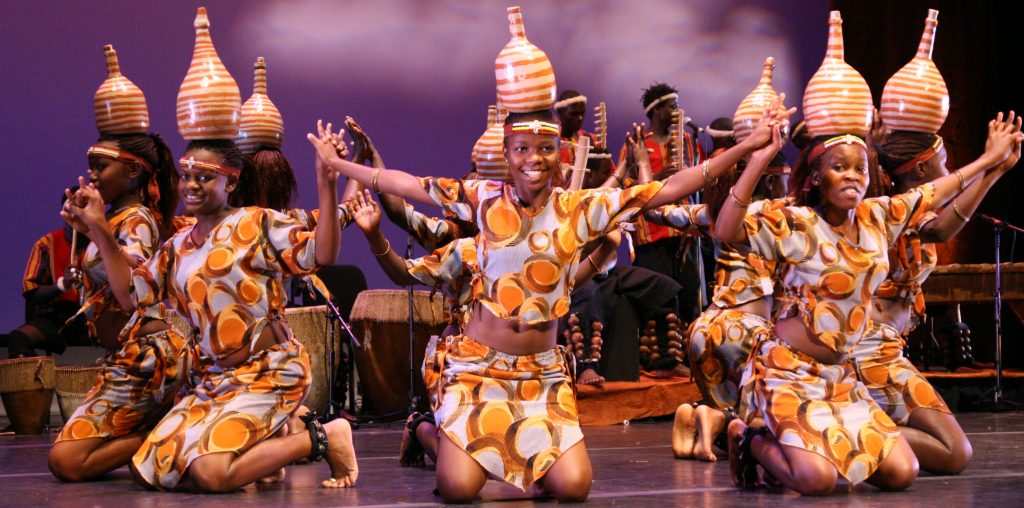 Uganda Culture Guide 29 Dancers in patterned outfits balance patterned pots on their heads on stage.