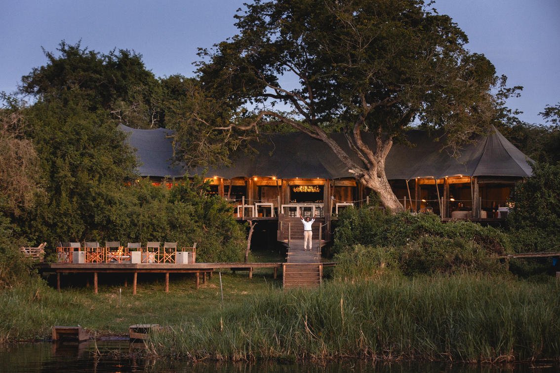 Luxury tented safari lodge illuminated at dusk by Akagera water's edge.