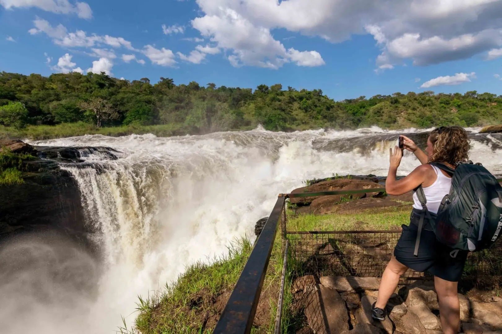 East Africa Safari Guide: Cost, Best Time & Routes 2026/2027 15 Traveler photographing the powerful Murchison Falls waterfall in Murchison Falls National Park, Uganda