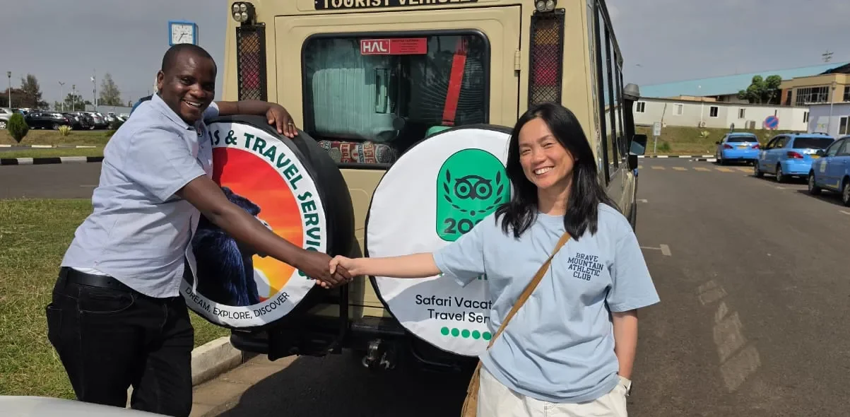 Ultimate Uganda Airport Guide: Best Travel Tips (2026/2027) 11 Safari Vacations and Travel Services Ltd representative welcoming an international traveler beside a safari vehicle during an airport transfer in Rwanda or Uganda