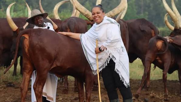 Uganda Culture Guide 7 A woman in traditional white attire posing with Ankole longhorn cattle.