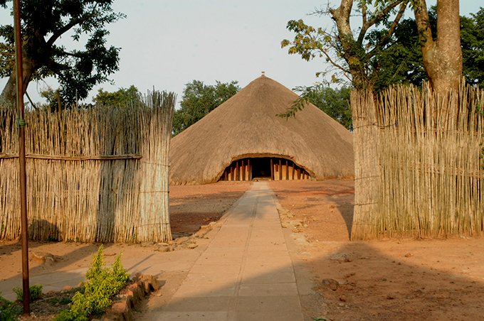 Uganda Culture Guide 23 Large traditional circular thatched building behind a split reed fence.