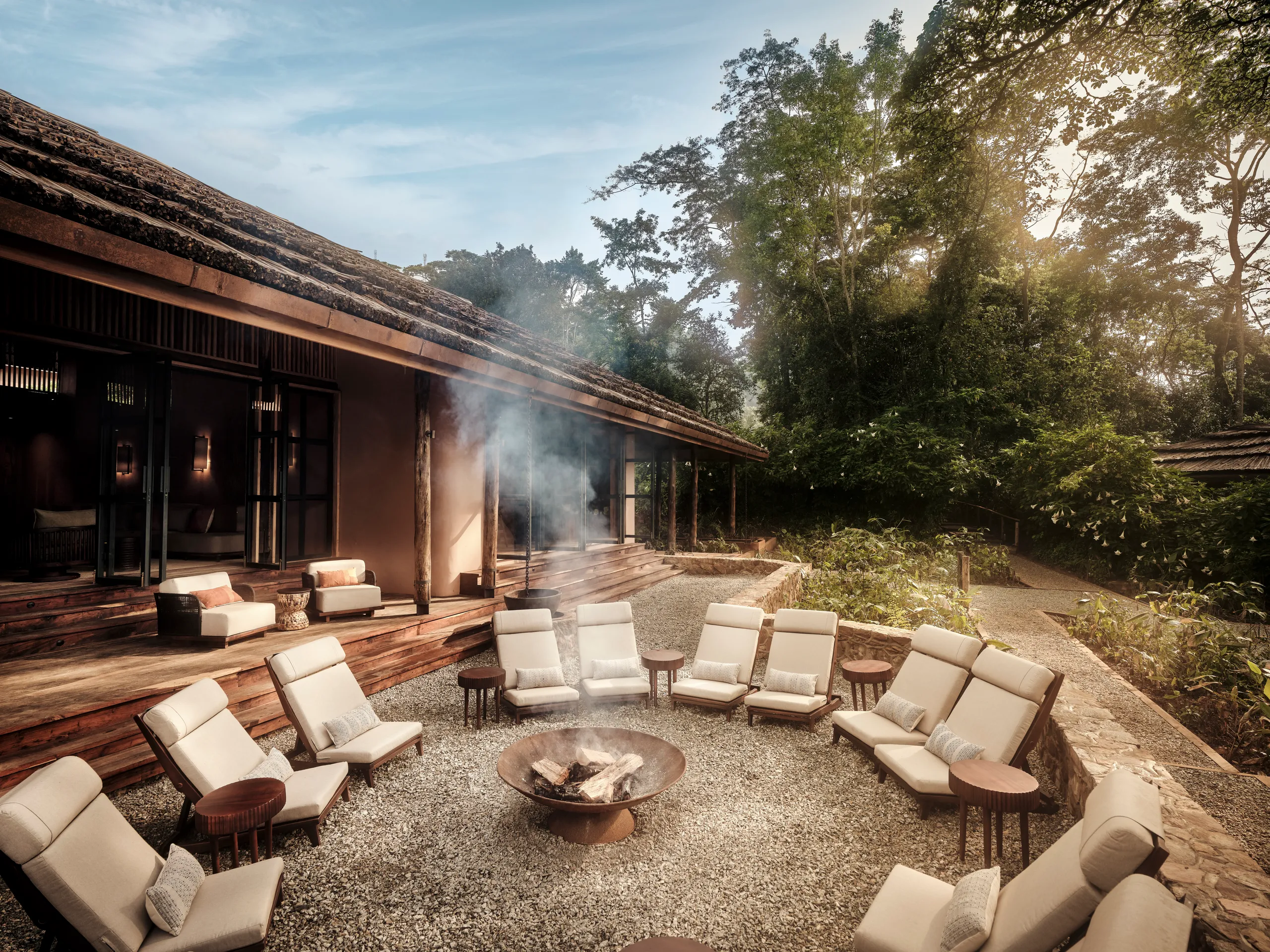 Gorilla Trekking Tips for First-Time Visitors 25 A luxury safari lodge courtyard in Uganda with comfortable lounge chairs arranged around a central fire pit near a dense jungle canopy