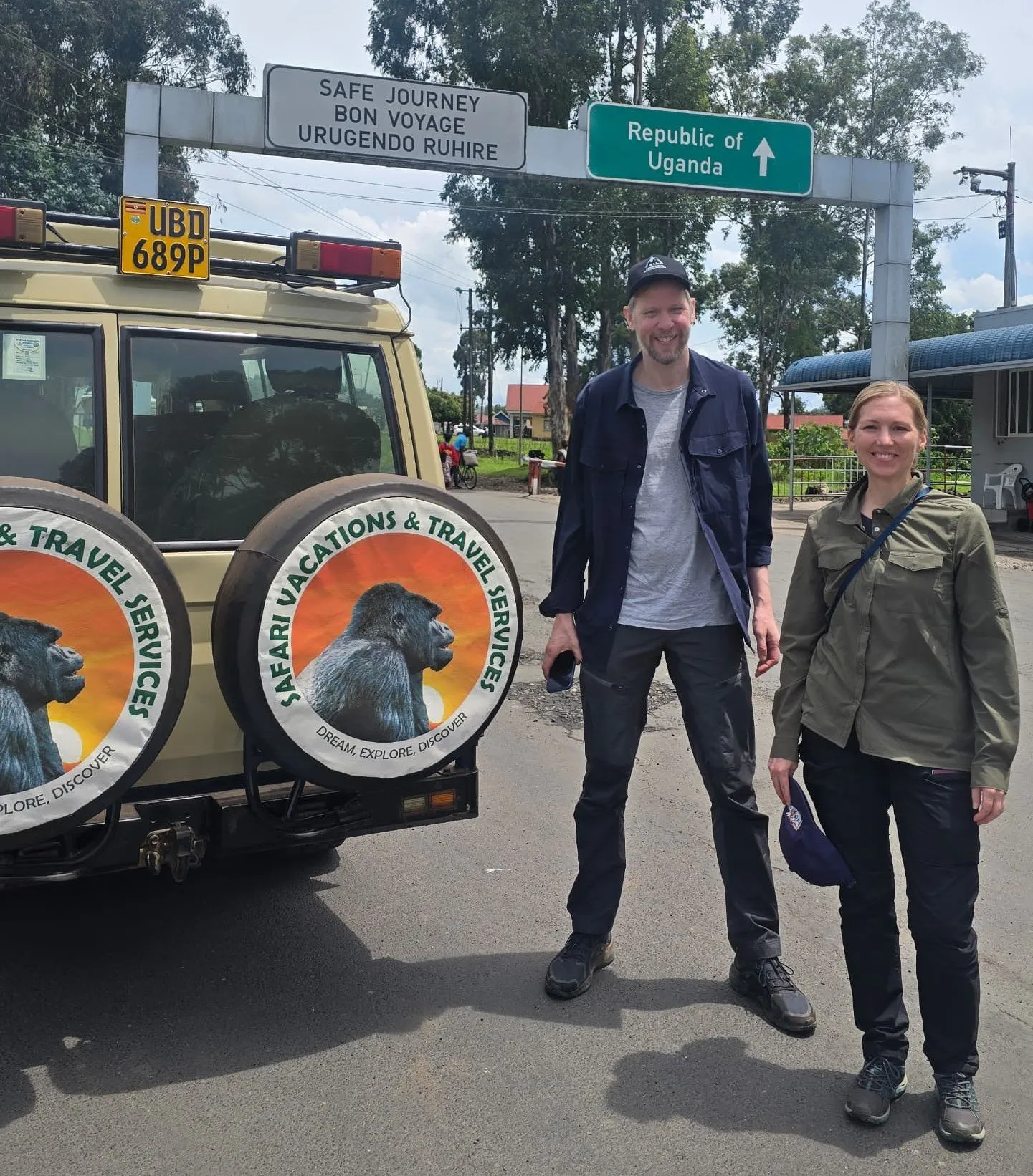 Ultimate Uganda Airport Guide: Best Travel Tips (2026/2027) 3 Travelers beside a Safari Vacations and Travel Services Ltd safari vehicle at the Rwanda Uganda border during a cross-border safari transfer