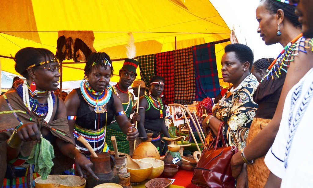 Uganda Culture Guide 1 Women in colorful Ugandan traditional attire showcase cultural items under a tent.(Uganda Culture Guide)