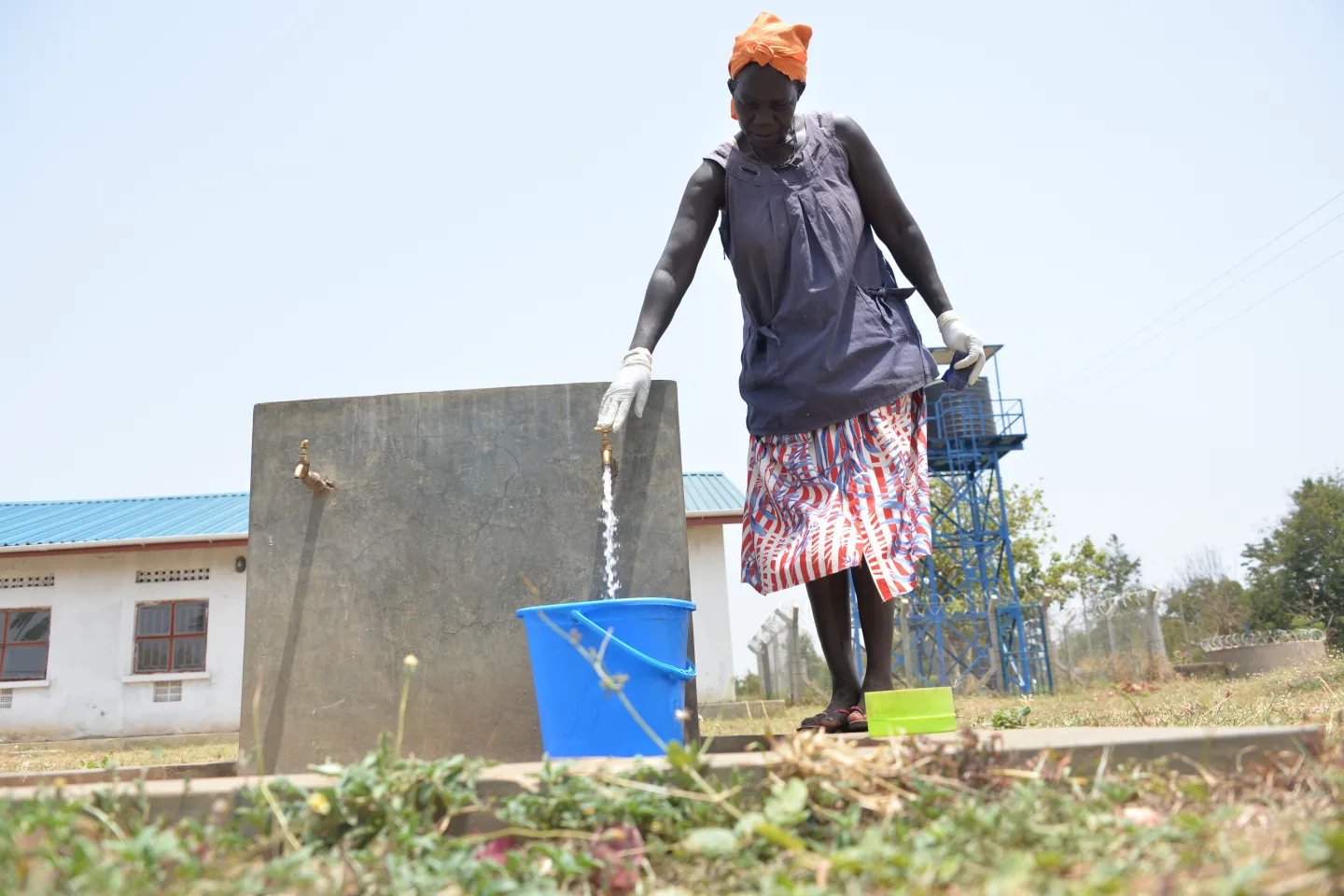 Uganda Safety Guide 5 A woman wearing protective gear fills a blue bucket from a clean water tap.